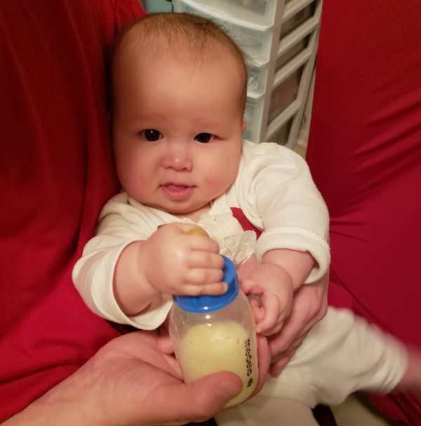 Baby holds bottle by nipple to show she is full