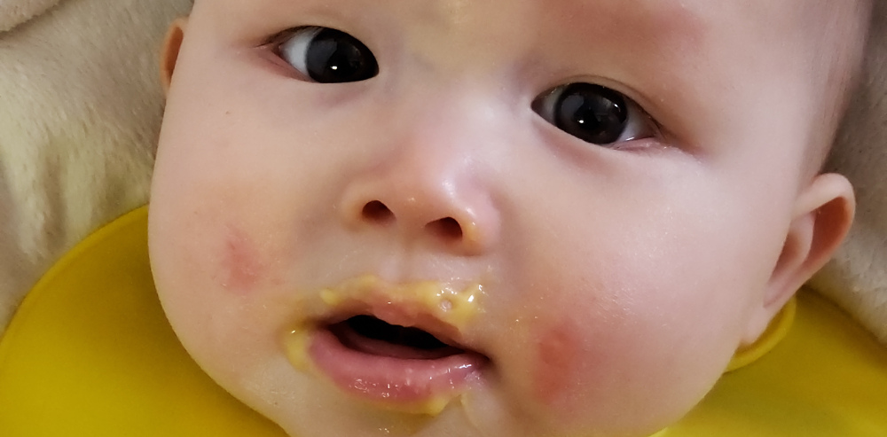 Close-up photo of baby with solid food around her mouth.