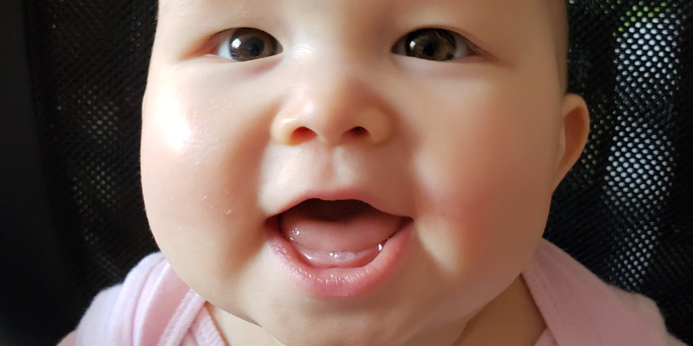 close of photo of smiling baby showing her first tooth.