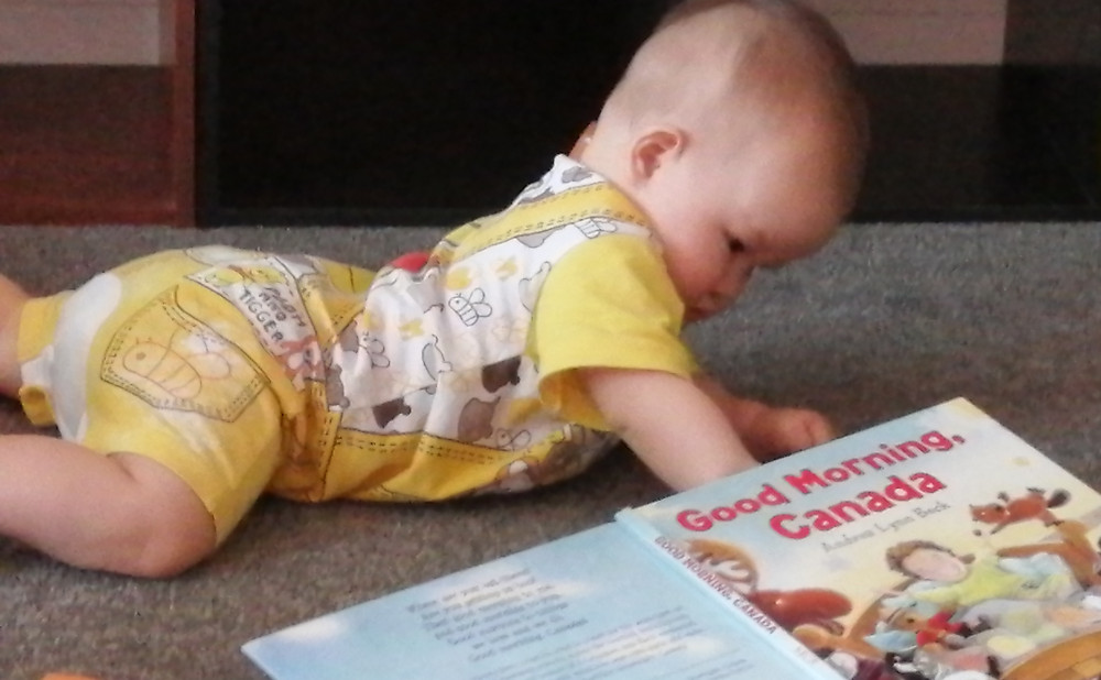 Baby Baobao examines the book, Good Morning, Canada, while crawling on floor