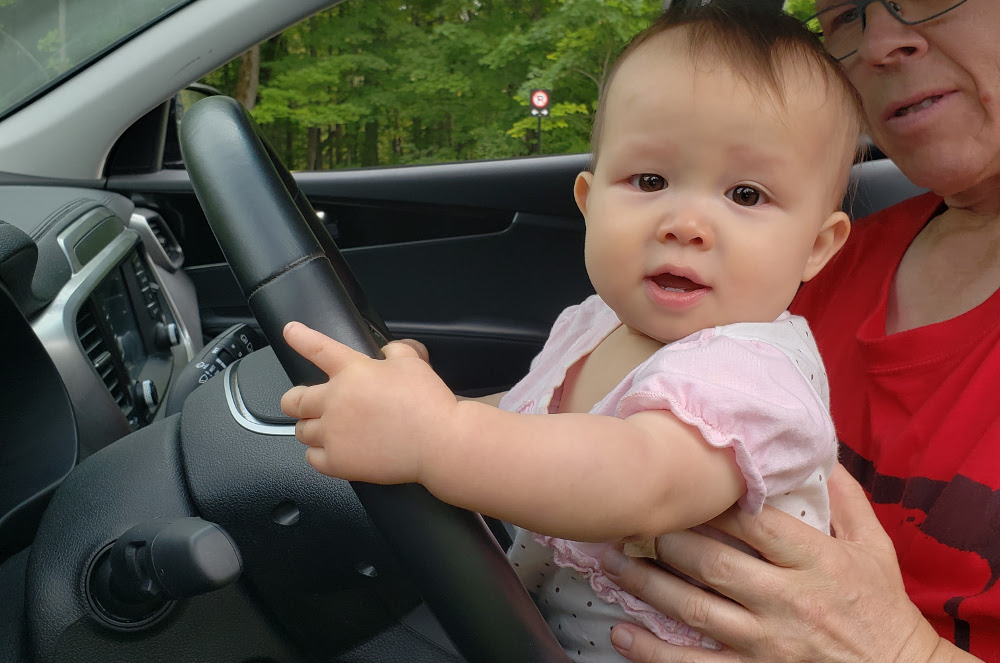 Photo of baby Baobao at the wheel of a car while sitting on Papa Zesser's lap.