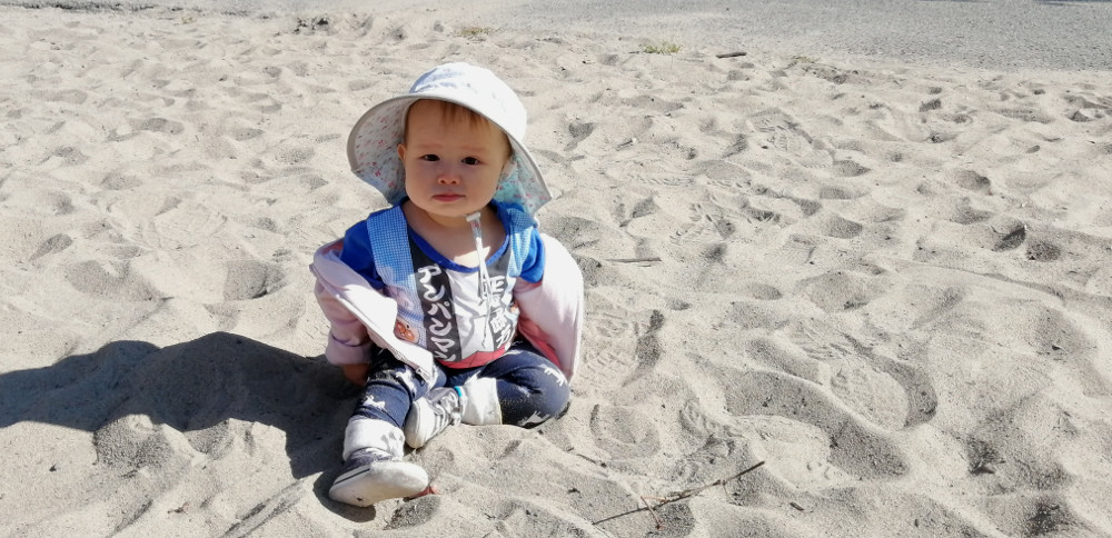 Photo of baby Baobao sitting in the sand of a playground while looking directly into the camera.